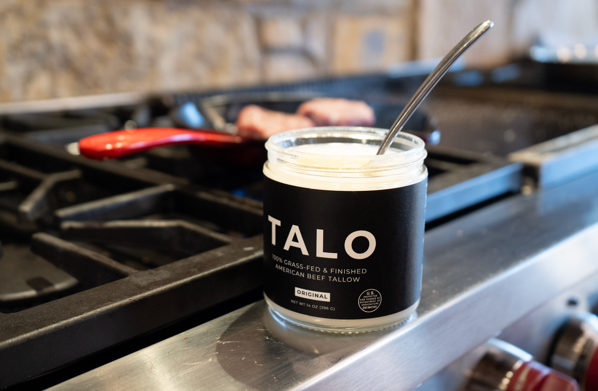Open TALO beef tallow jar with a spoon on a stove while cooking in a pan