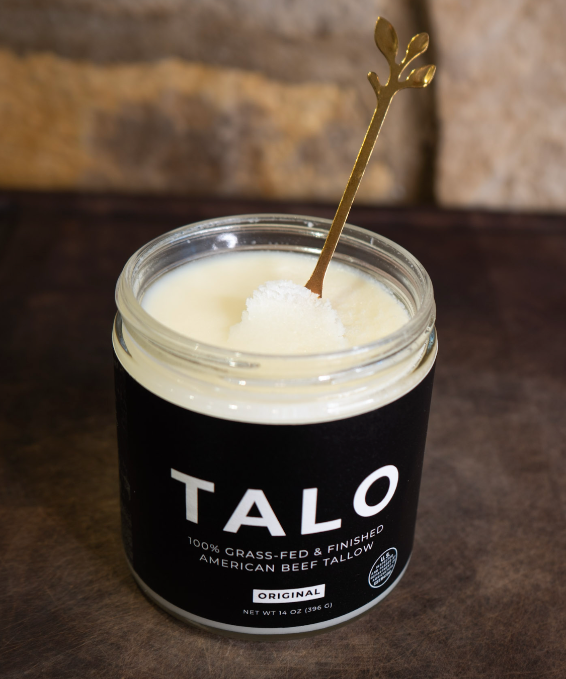 Open jar of TALO grass-fed beef tallow showing the creamy white tallow, with a gold spoon